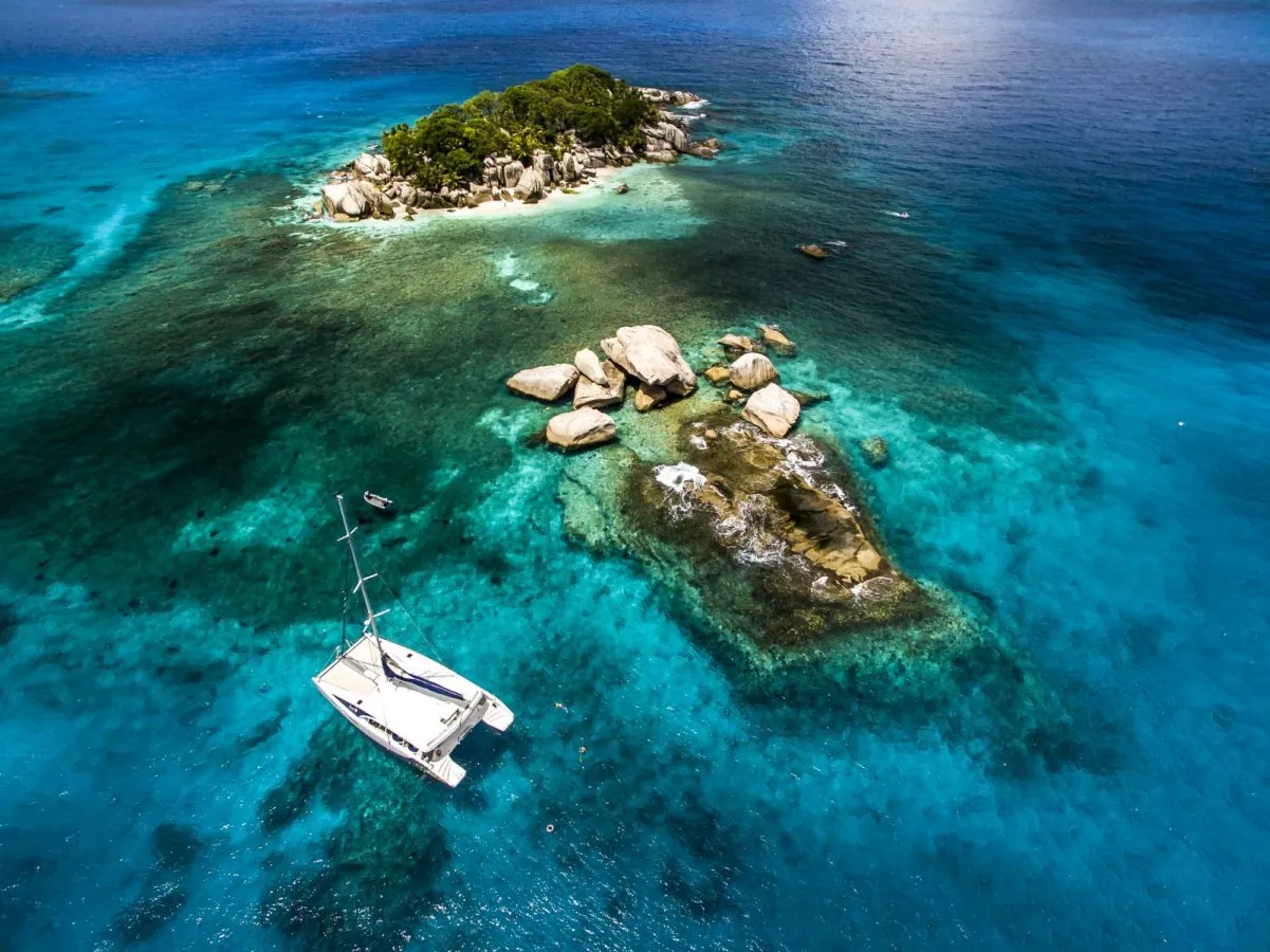 Aerial view of an islet and its reef with the catamaran nearby