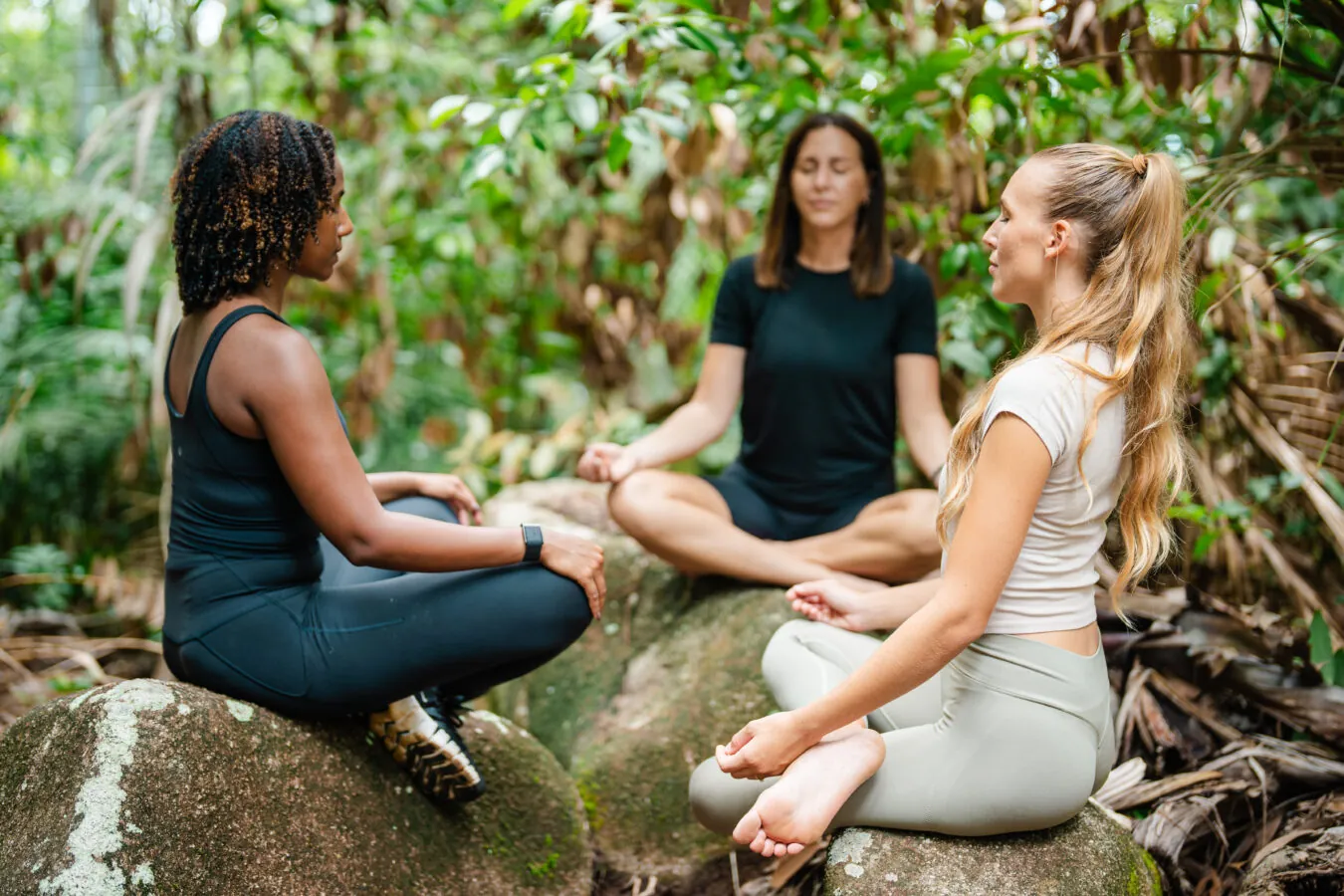 Three women meditating on a rock in the forest